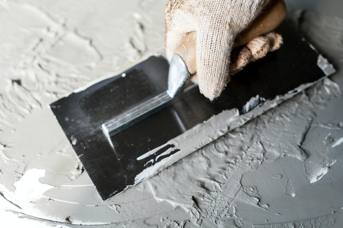 Grey plater being spread out with a plastering tool held by a gloved hand.